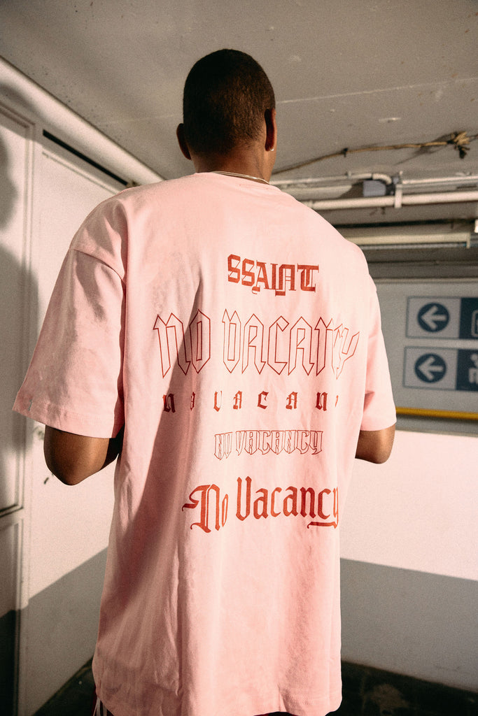 Person wearing a pink t-shirt with text on the back, standing in an indoor setting.